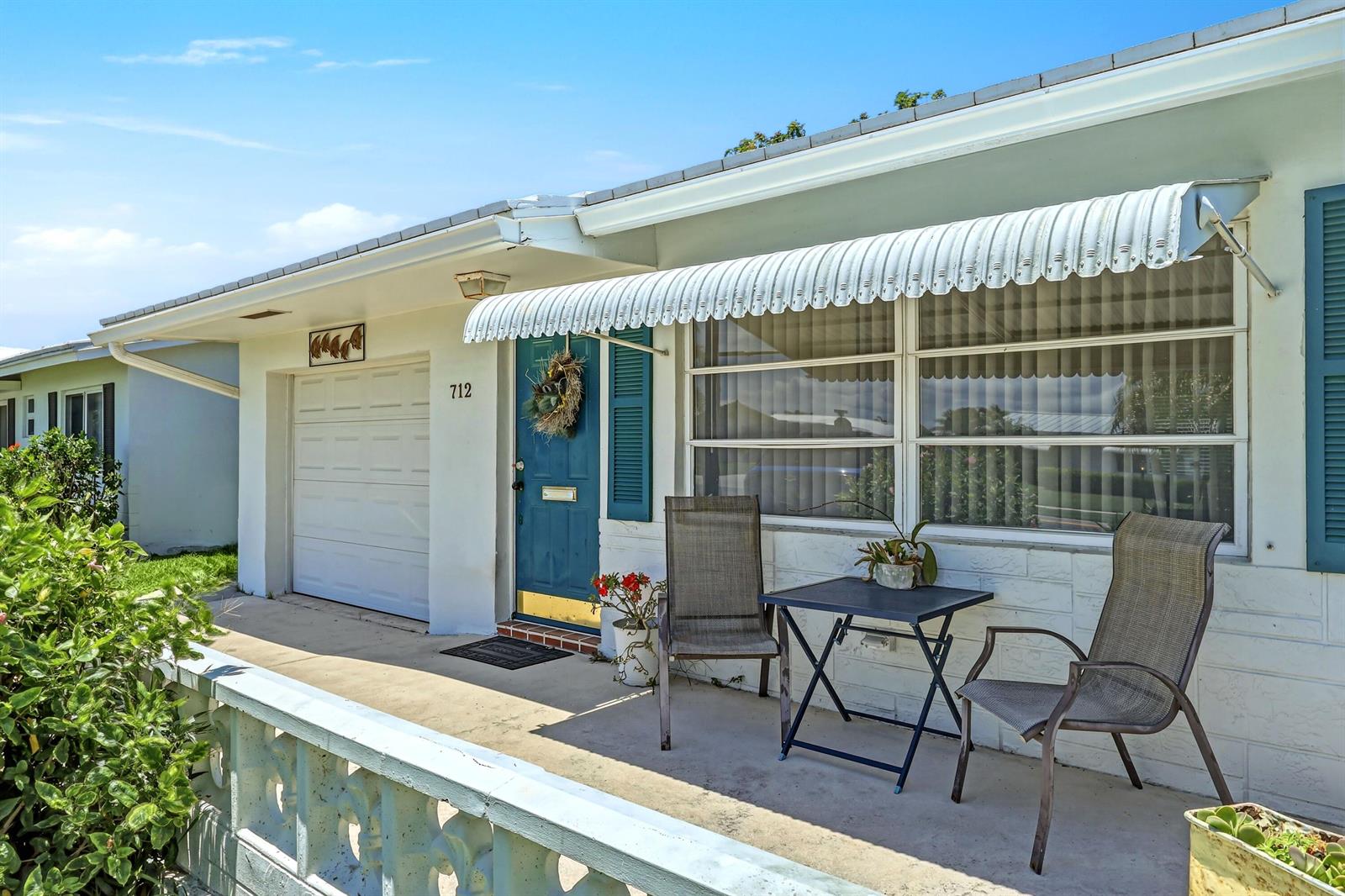A white house exterior features a blue front door, a metal awning, and patio furniture — 712 SW 18th Street, Boynton Beach FL 33426, BOYNTON BEACH, FL