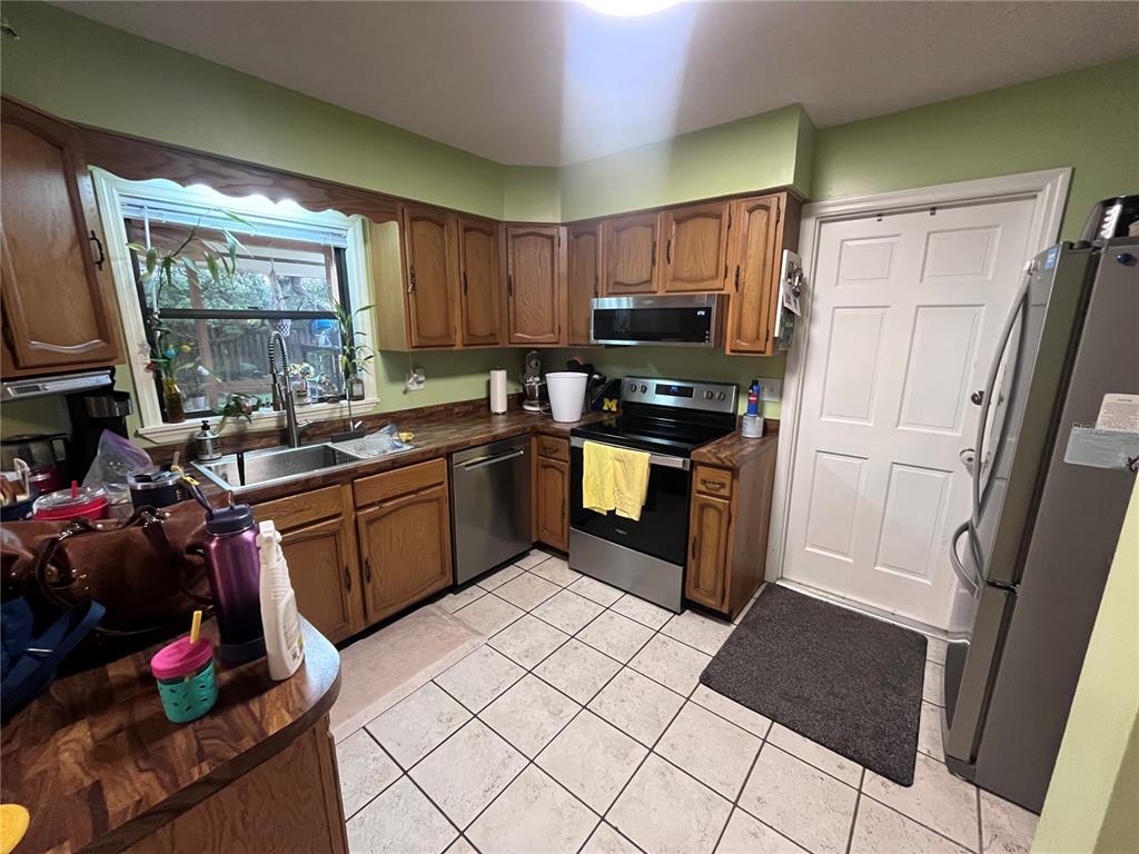 A kitchen features wood cabinets, a stainless steel stove, a dishwasher, and light-colored tile flooring — 2117 YORKSHIRE DRIVE, DELAND, FL