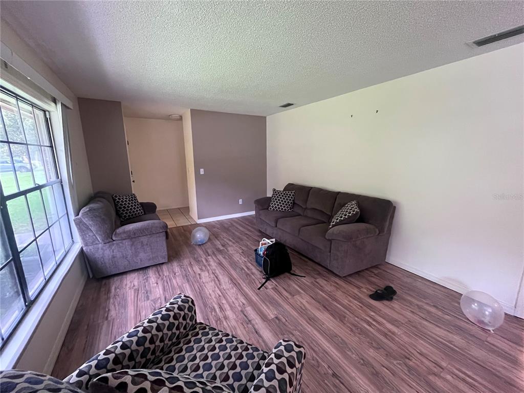 A living room features wood-look flooring, a large window, and three pieces of upholstered furniture — 2117 YORKSHIRE DRIVE, DELAND, FL