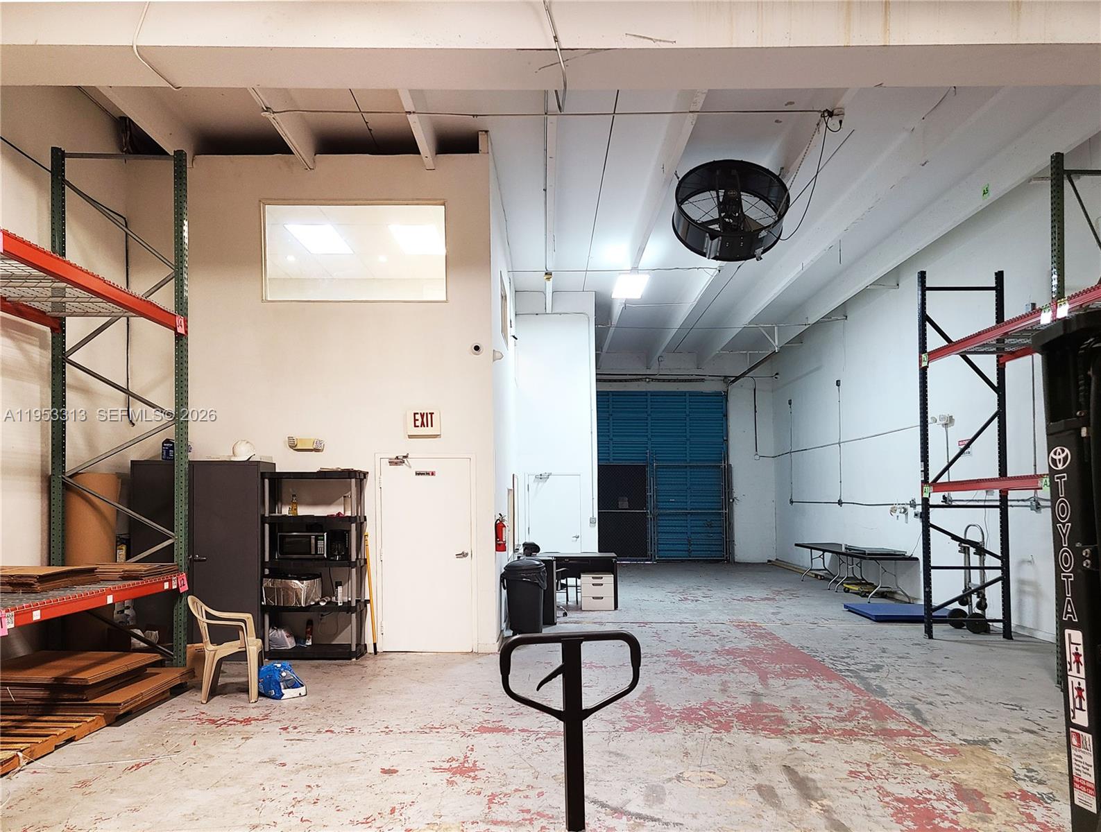 This industrial warehouse space features concrete floors, metal shelving units, and a ceiling-mounted fan — 7344 NW 56th St # 7344, Miami FL 33166, MIAMI, FL