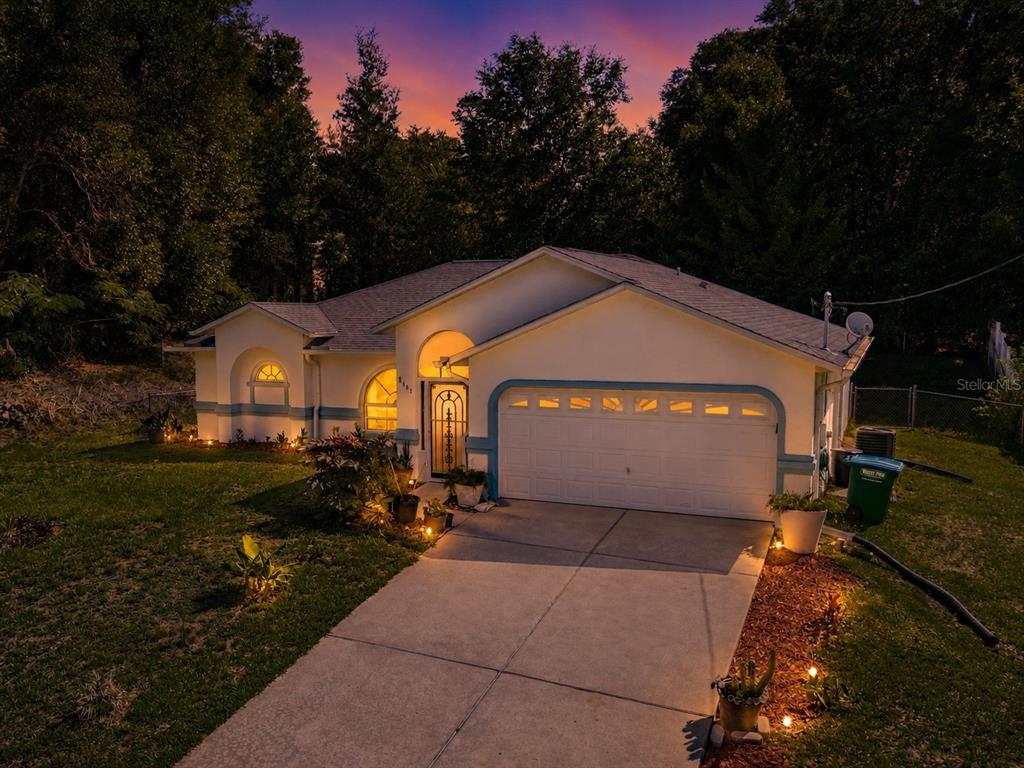 A single-story house with a white garage and arched windows at twilight — 8461 N TITLEIST DRIVE, CITRUS SPRINGS, FL