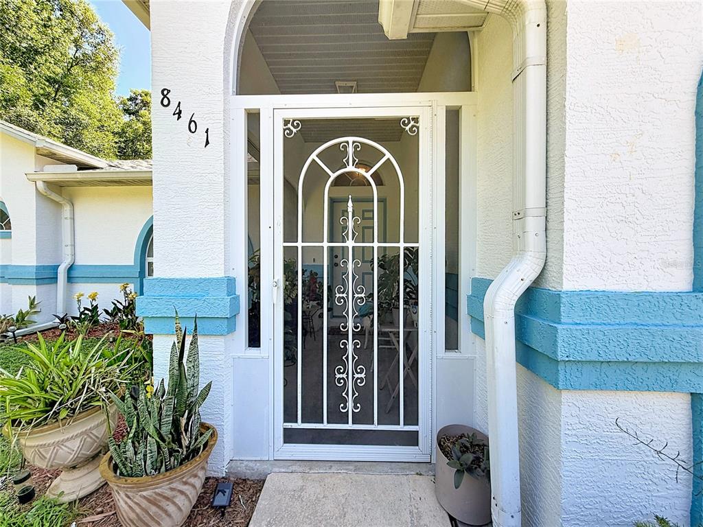 A white security screen door is centered on the front porch of a stucco house — 8461 N TITLEIST DRIVE, CITRUS SPRINGS, FL