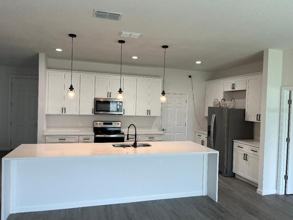 A kitchen features white cabinets, a large island with a sink, and stainless steel appliances — 611 AMAZON PLACE, KISSIMMEE, FL