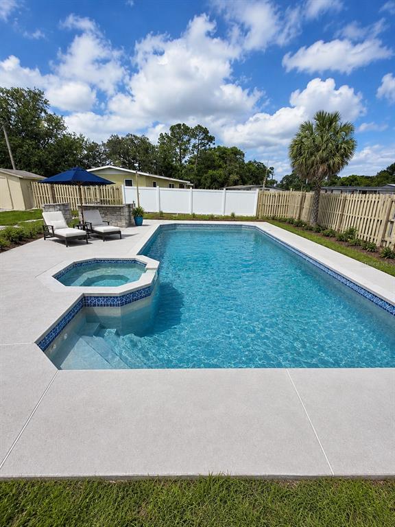 A swimming pool with an attached spa sits in a backyard with a white fence — 802 CRAWFORD STREET, DELTONA, FL