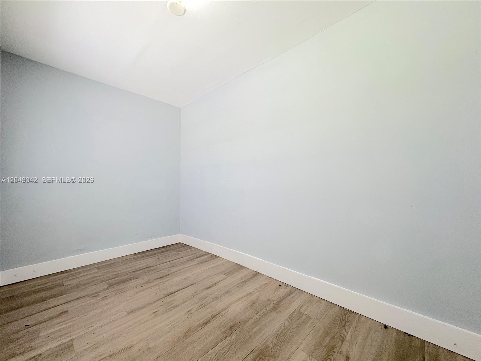 An empty room features light blue walls, white baseboards, and wood-look laminate flooring — 1825 Mckinley St # 2, Hollywood FL 33020, HOLLYWOOD, FL