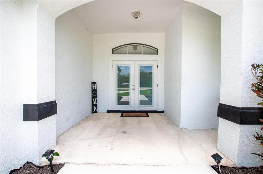 A covered entryway features a white double door with a transom window and a HOME sign — 3442 NE APPALOOSA STREET, ARCADIA, FL