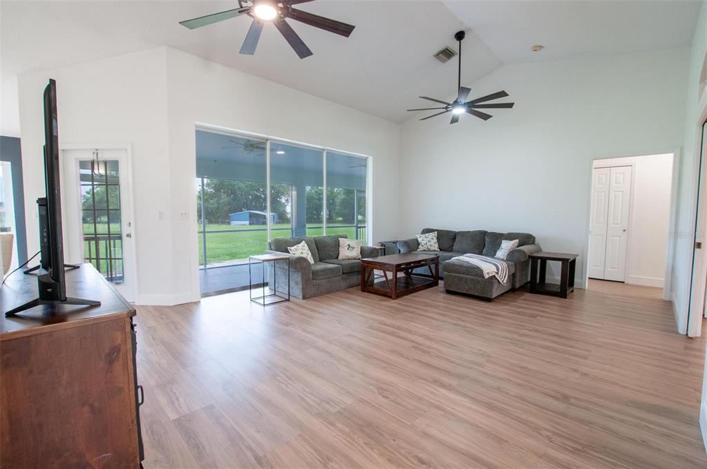 A living room with light wood floors, two ceiling fans, and a large sliding glass door — 3442 NE APPALOOSA STREET, ARCADIA, FL