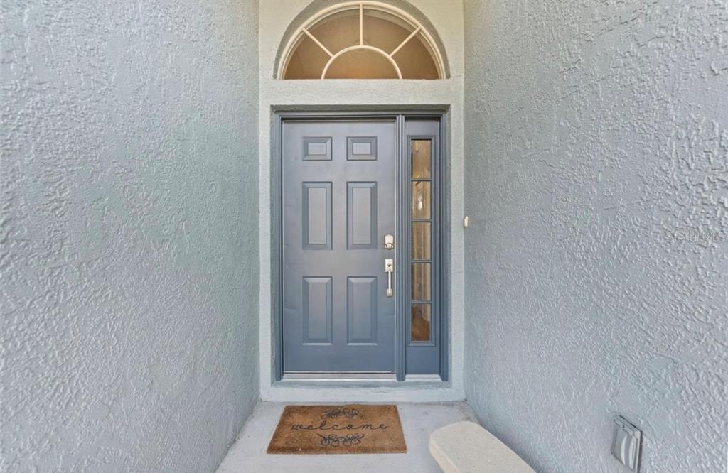 A gray front door with a side window and arched transom sits in a recessed entryway — 12910 VICKSBURG DRIVE, TAMPA, FL