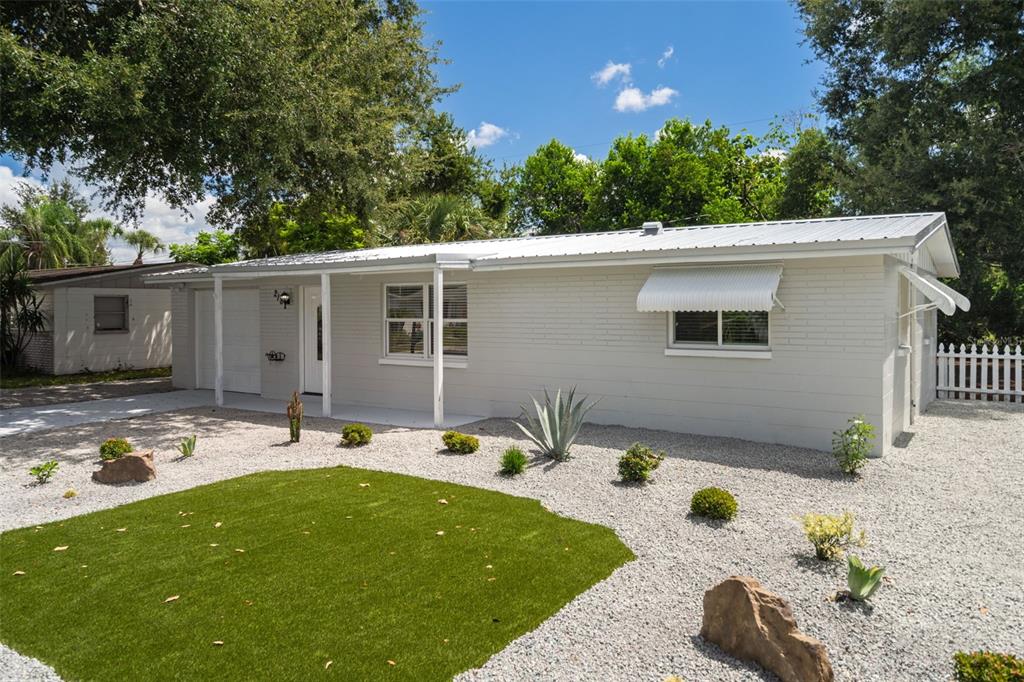 A single-story house with a white brick exterior, metal roof, and a gravel front yard — 2187 DIXIE GARDEN LOOP, HOLIDAY, FL