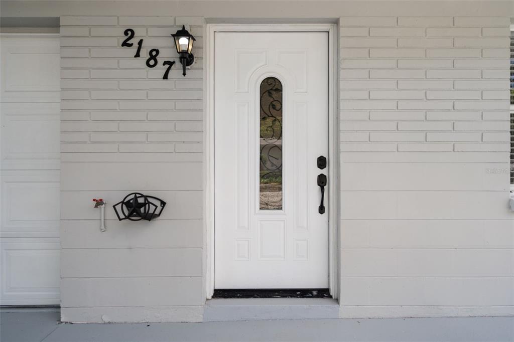 A white front door with a decorative glass insert is set into a light-colored brick wall — 2187 DIXIE GARDEN LOOP, HOLIDAY, FL