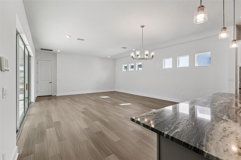 An open-concept living area features light wood-look flooring, white walls, and a modern chandelier — 10757 TORCHWOOD SEA WAY, SAN ANTONIO, FL