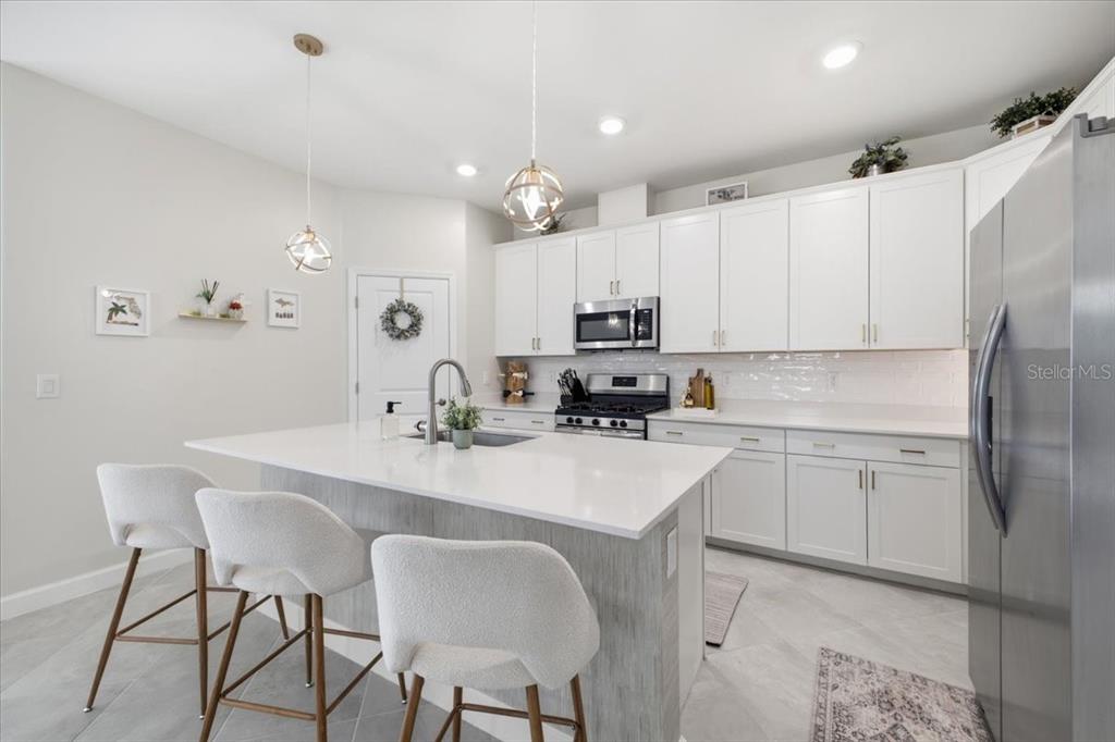 A modern kitchen features white cabinetry, a quartz-topped island with bar seating, and stainless appliances — 5250 CORAL REEF WAY, LAKEWOOD RANCH, FL
