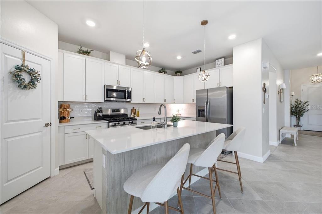 A modern kitchen features white cabinetry, a central island with bar seating, and stainless appliances — 5250 CORAL REEF WAY, LAKEWOOD RANCH, FL
