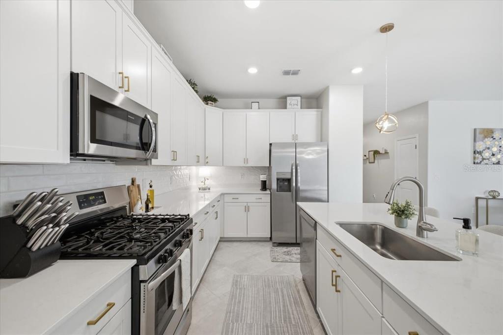 A modern kitchen features white cabinetry, stainless steel appliances, and a large quartz-topped island — 5250 CORAL REEF WAY, LAKEWOOD RANCH, FL