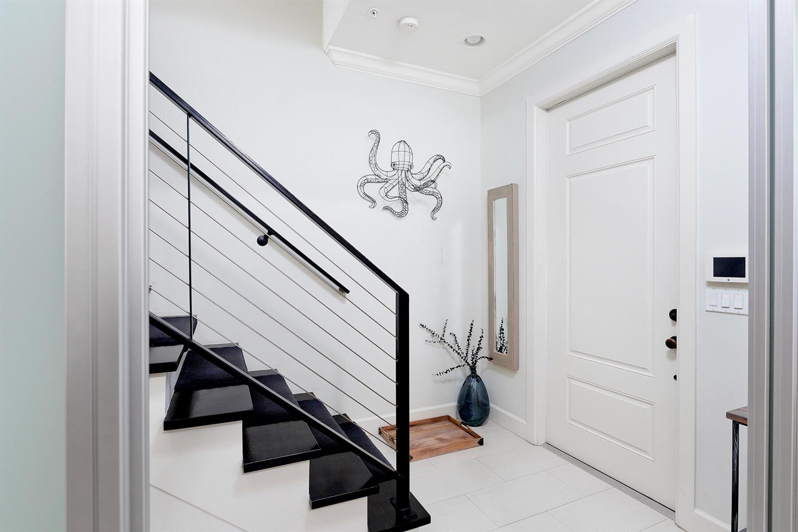 A modern entryway features a black staircase with cable railings, white tile floors, and decor — 362 W Cannery Row Circle, Delray Beach FL 33444, DELRAY BEACH, FL