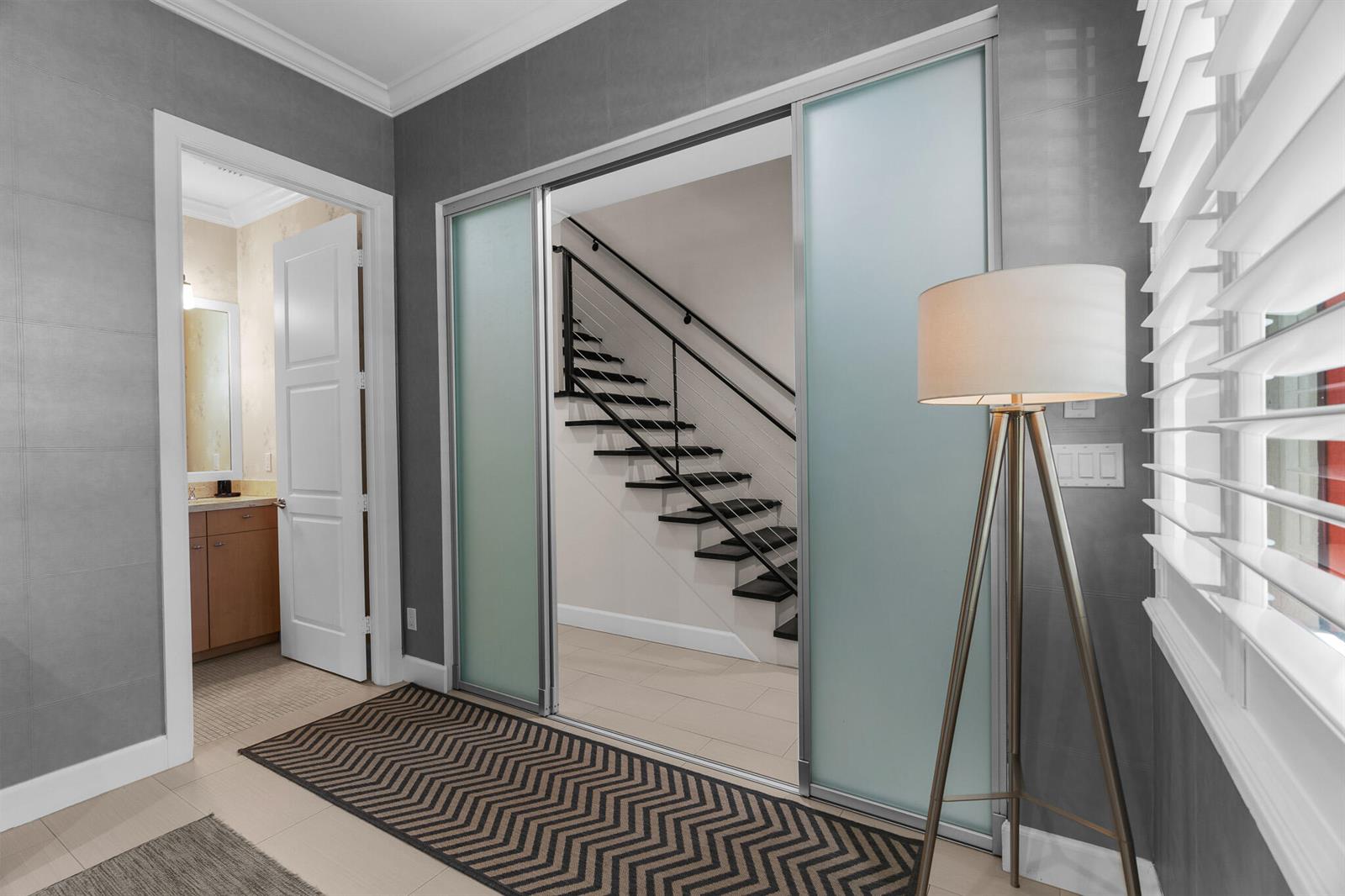 A hallway features a frosted glass sliding door, a modern staircase, and a floor lamp — 362 W Cannery Row Circle, Delray Beach FL 33444, DELRAY BEACH, FL