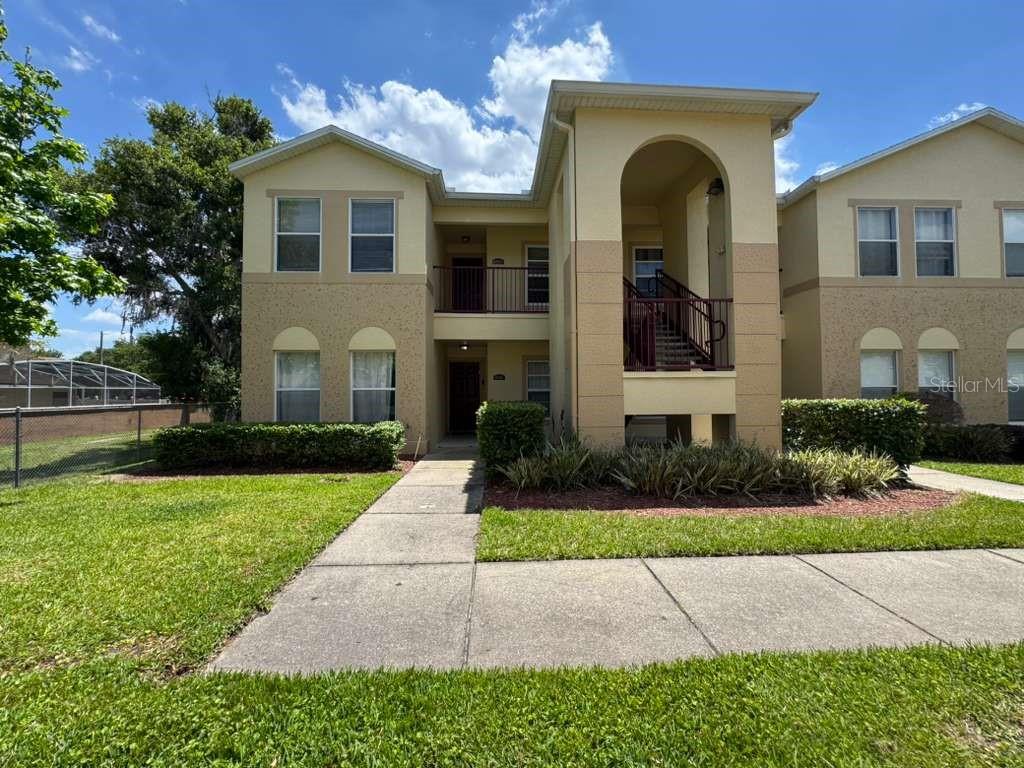 A two-story apartment building exterior with tan stucco walls, arched entryway, and a concrete walkway — 2866 CLUB CORTILE CIRCLE UNIT B, KISSIMMEE, FL