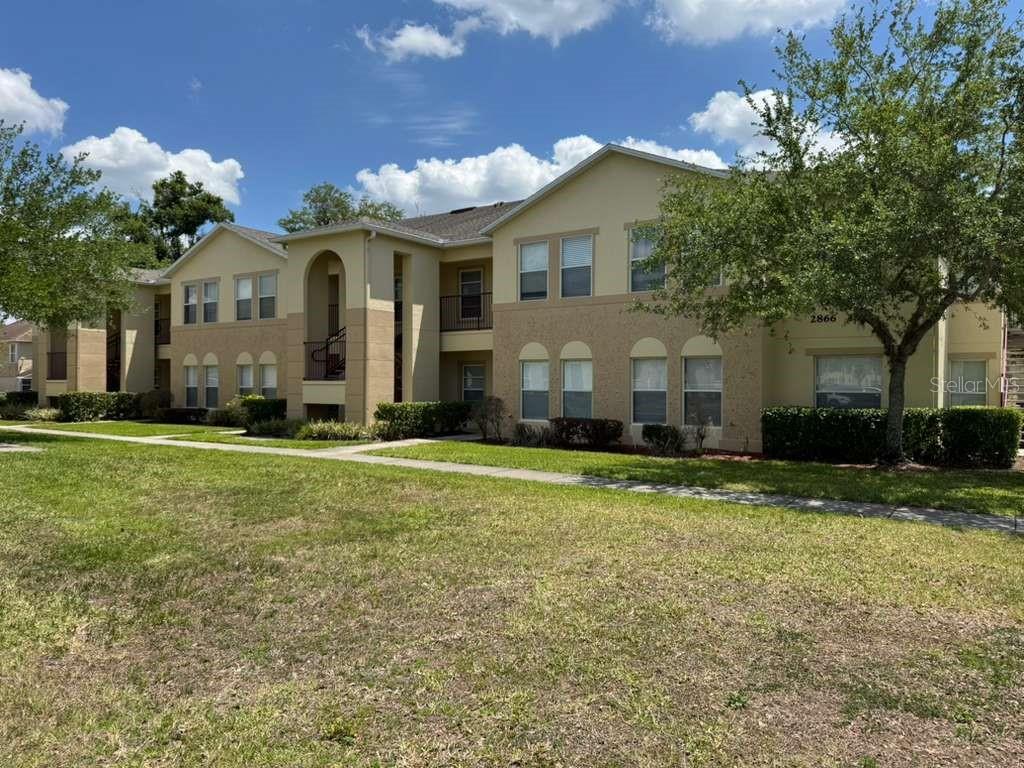 A two-story apartment building with beige stucco siding and a grassy lawn in front — 2866 CLUB CORTILE CIRCLE UNIT B, KISSIMMEE, FL