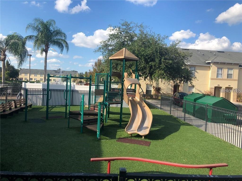 A playground with a slide and climbing structure sits on a green turf area — 2866 CLUB CORTILE CIRCLE UNIT B, KISSIMMEE, FL