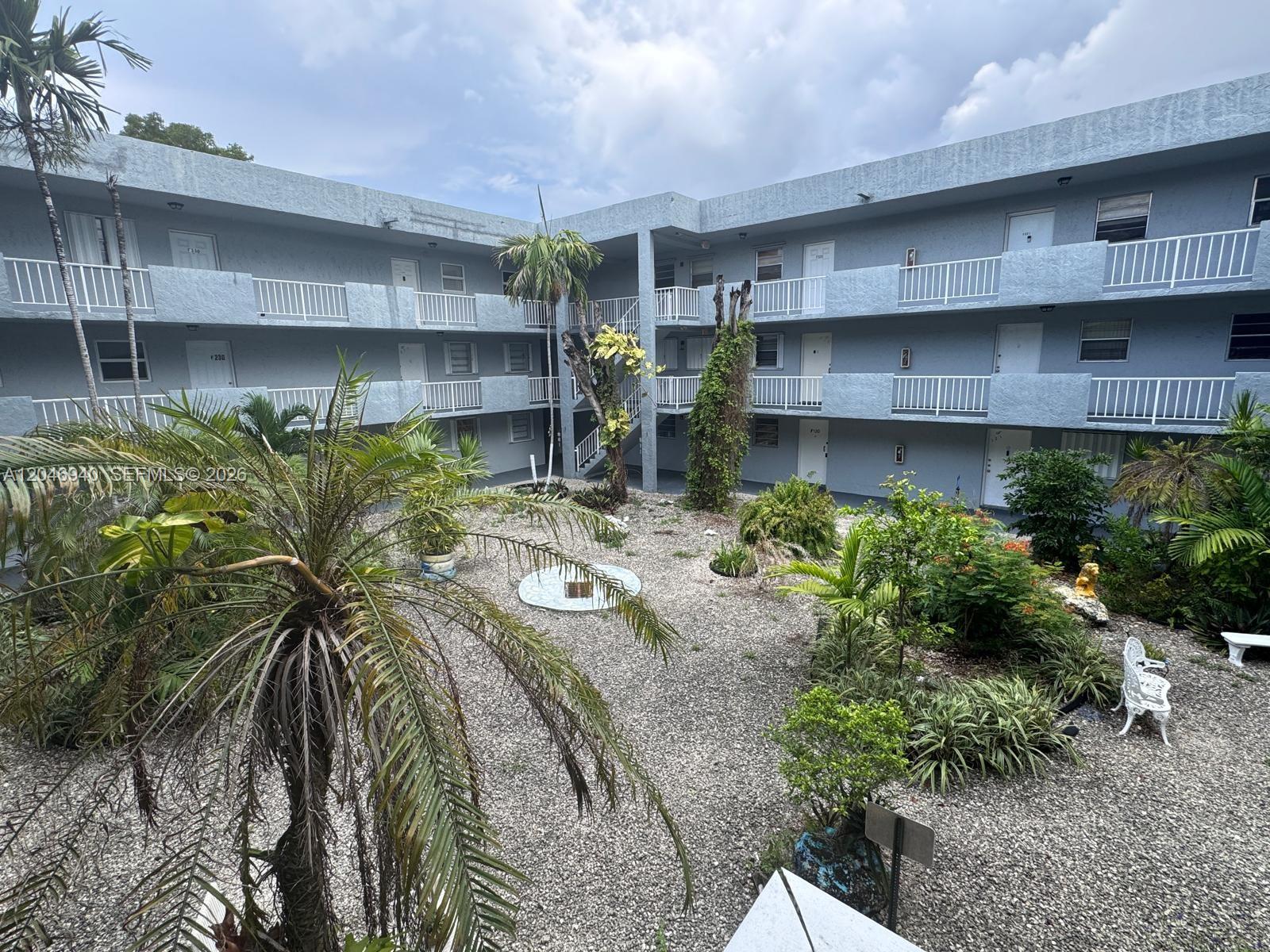 An exterior view of a multi-story apartment building courtyard with gravel landscaping and palm trees — 1725 W 60th St # F222, Hialeah FL 33012, HIALEAH, FL