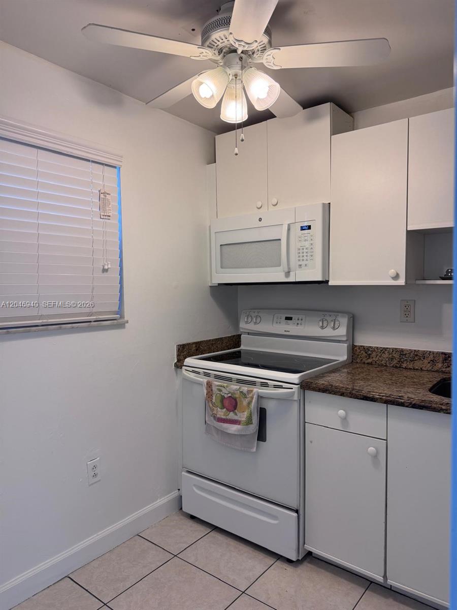 A kitchen features white cabinets, a white stove, a microwave, and granite countertops — 1725 W 60th St # F222, Hialeah FL 33012, HIALEAH, FL
