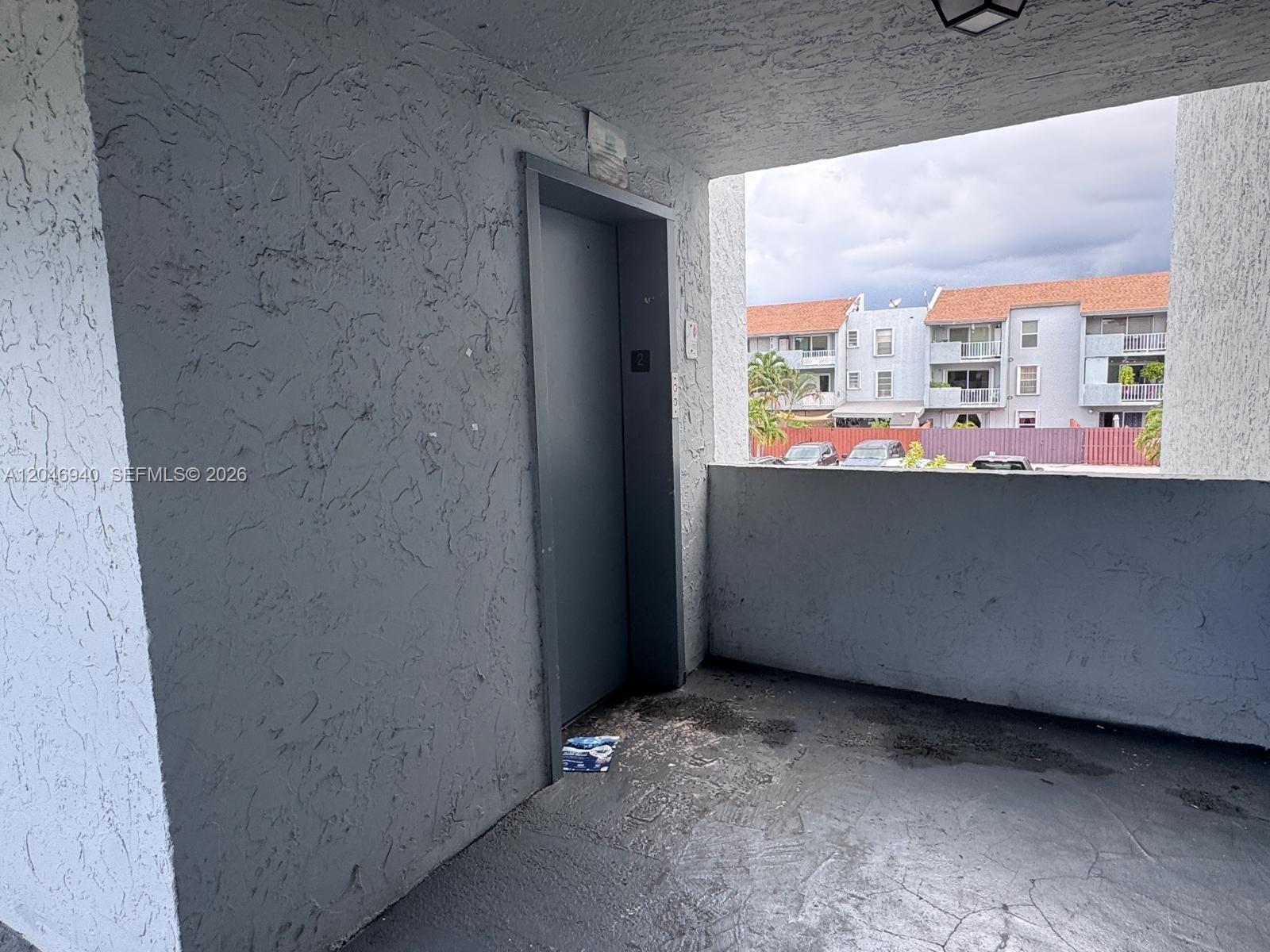 An outdoor balcony features a gray door, textured walls, and a view of apartment buildings — 1725 W 60th St # F222, Hialeah FL 33012, HIALEAH, FL