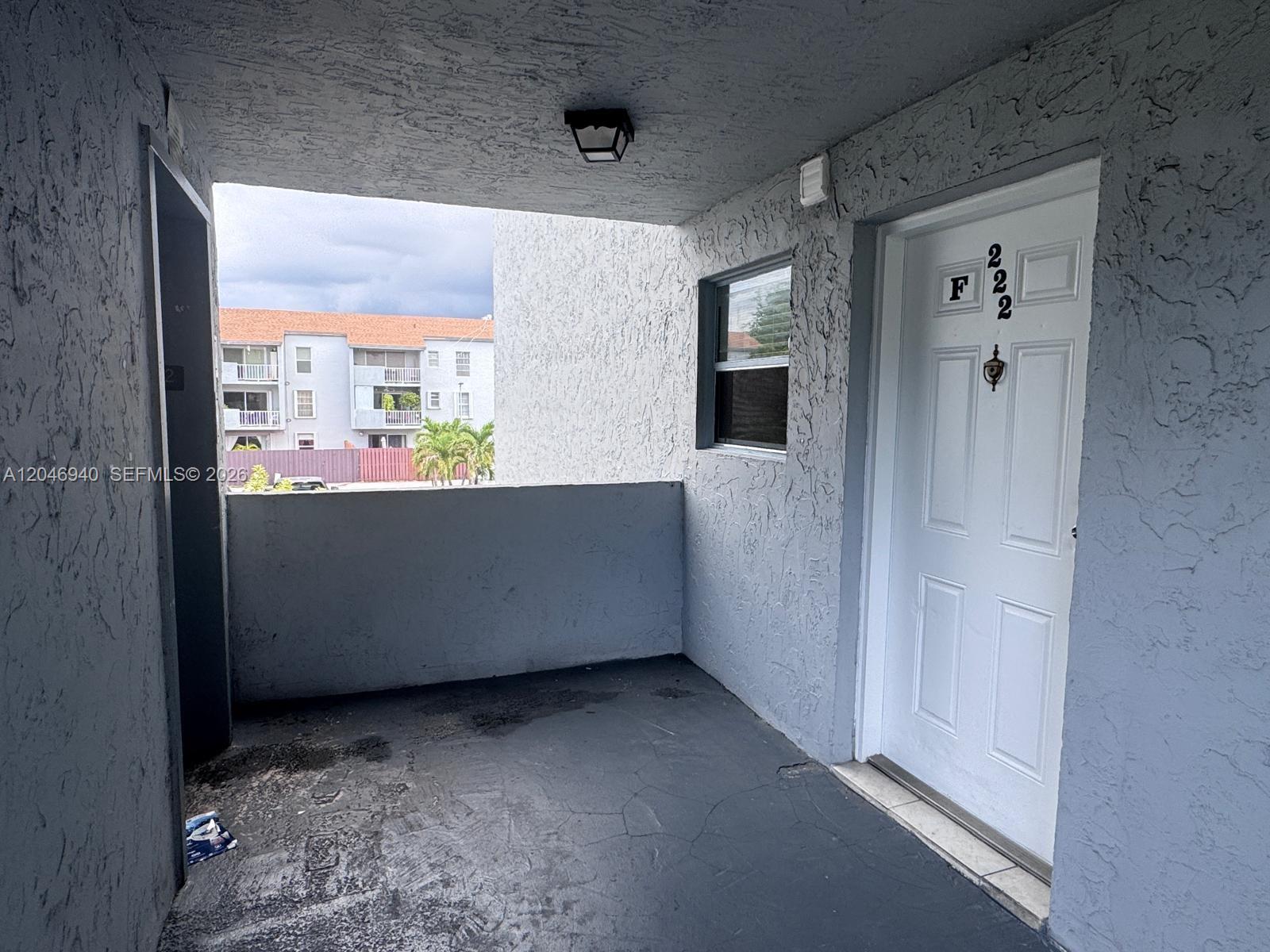 A gray stucco balcony features a white door labeled F222 and a small window — 1725 W 60th St # F222, Hialeah FL 33012, HIALEAH, FL