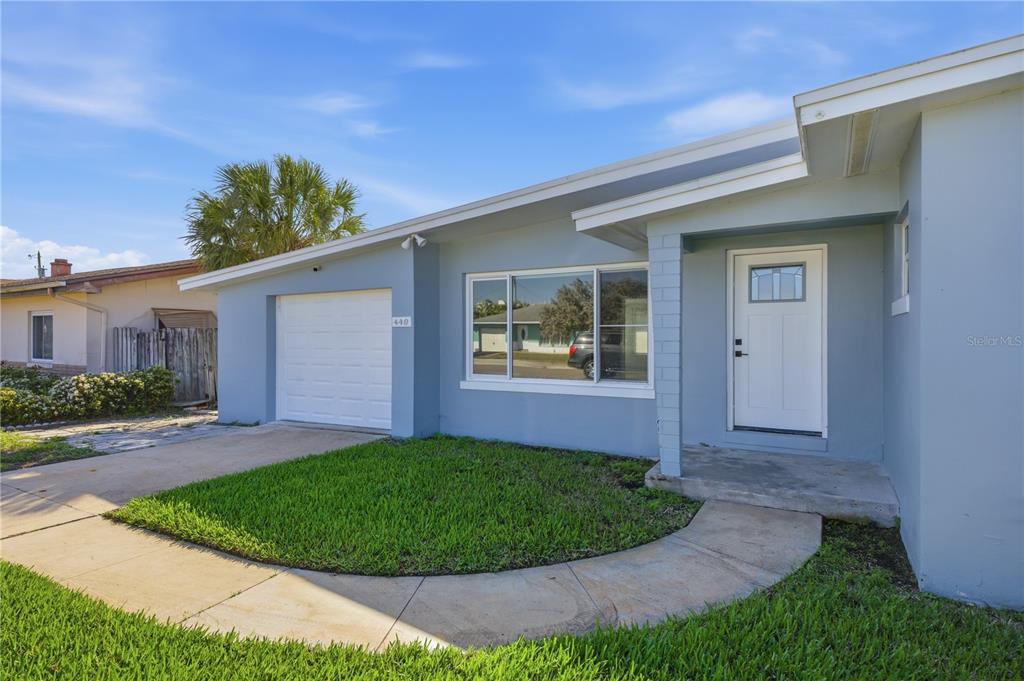 A light blue single-story house features a white garage door, a front door, and landscaping — 440 89TH AVENUE, ST PETE BEACH, FL