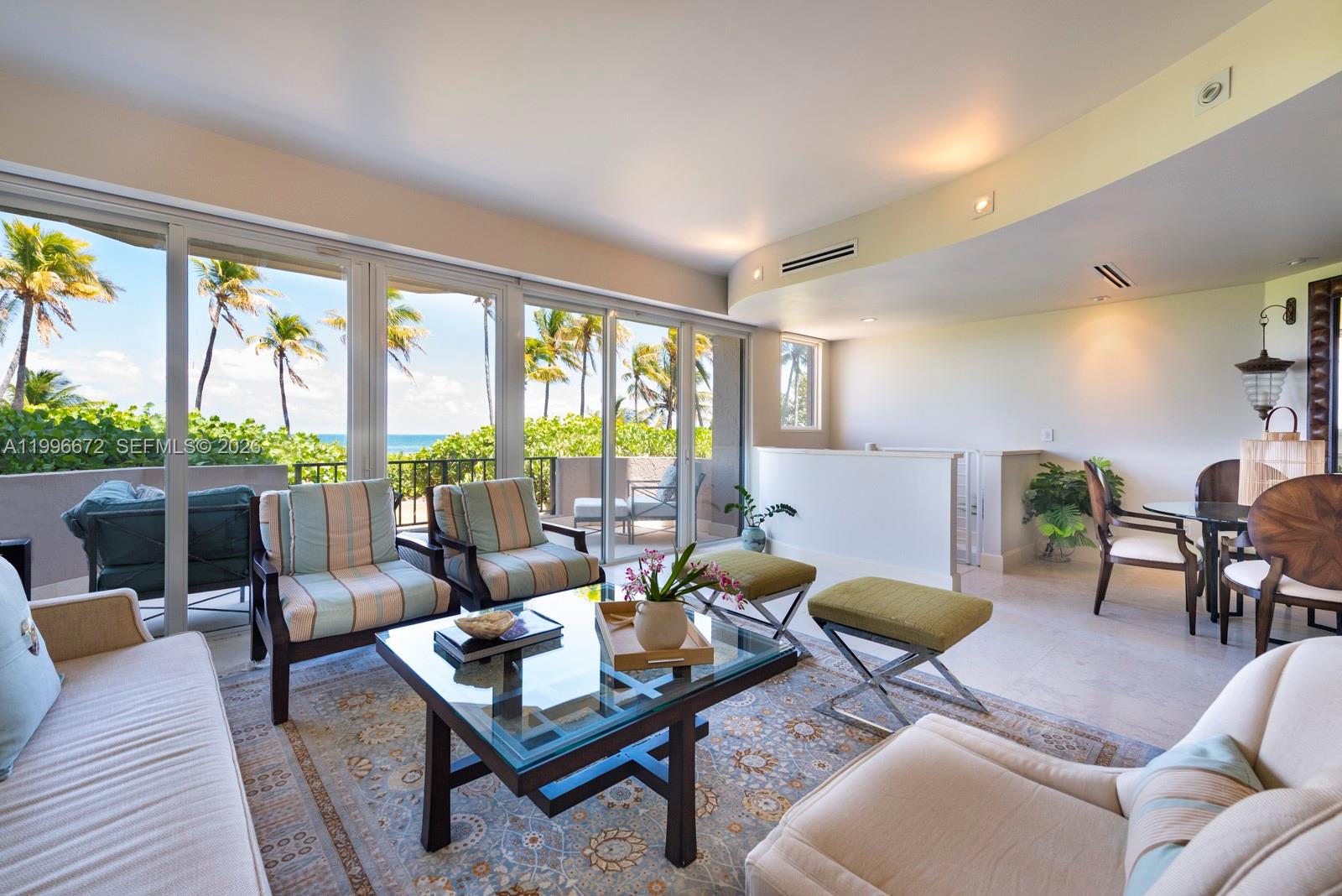 A living room features a glass coffee table, striped armchairs, and floor-to-ceiling windows overlooking palm trees — 201 Crandon Blvd # 174, Key Biscayne FL 33149, KEY BISCAYNE, FL