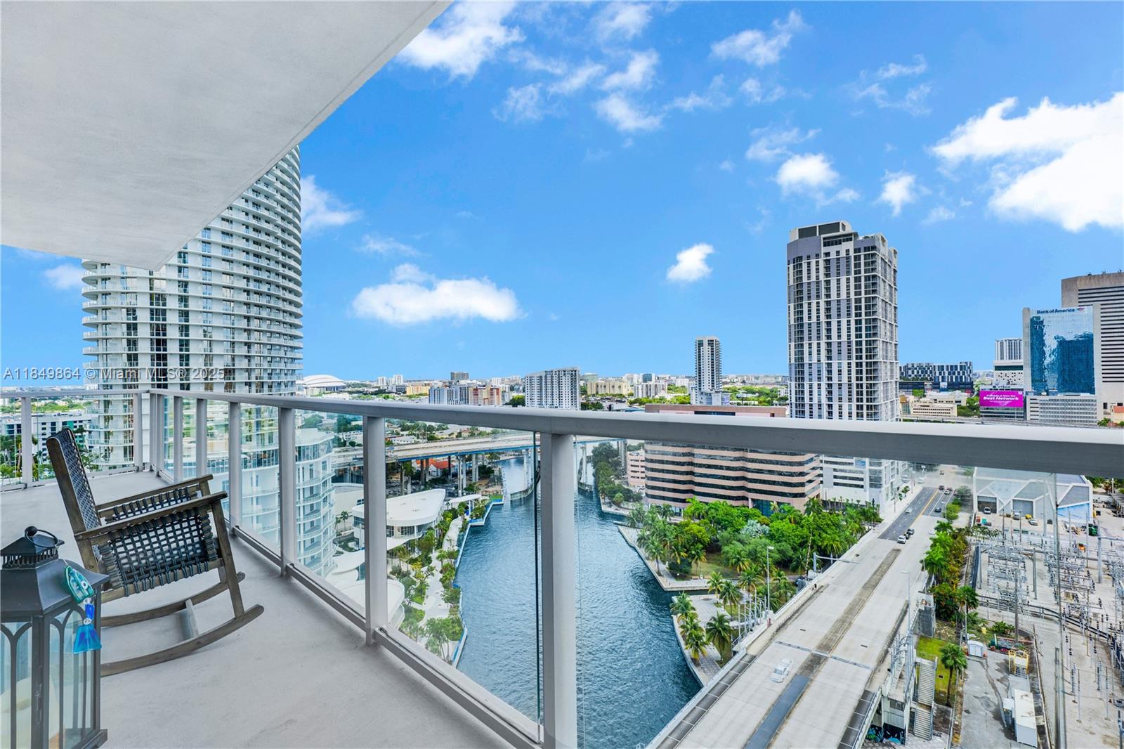 A high-rise balcony with a rocking chair overlooks a river, city skyline, and highway — 185 SW 7th St # 1901, Miami FL 33130, MIAMI, FL