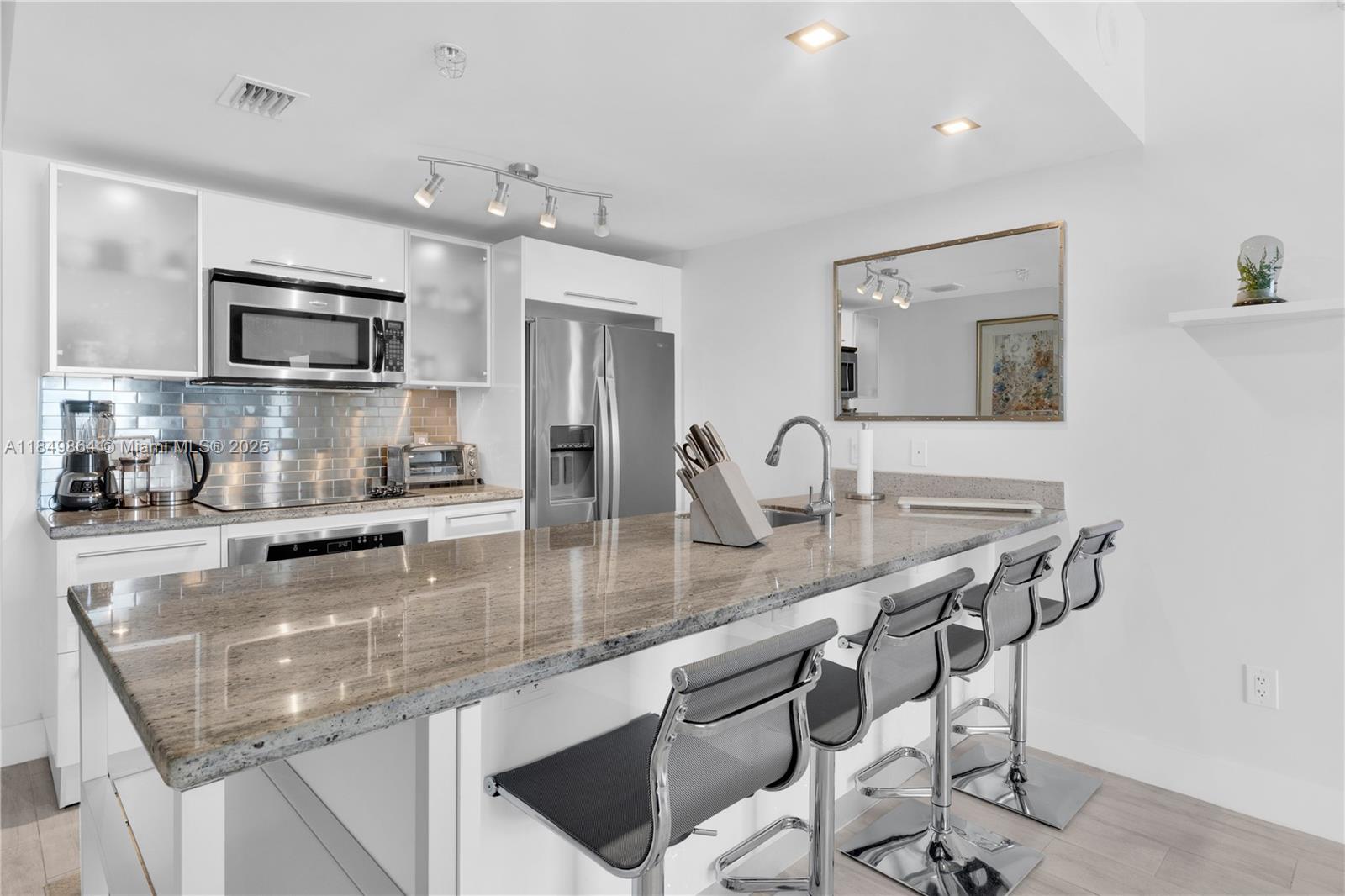 A modern kitchen features white cabinetry, stainless steel appliances, and a granite-topped breakfast bar — 185 SW 7th St # 1901, Miami FL 33130, MIAMI, FL