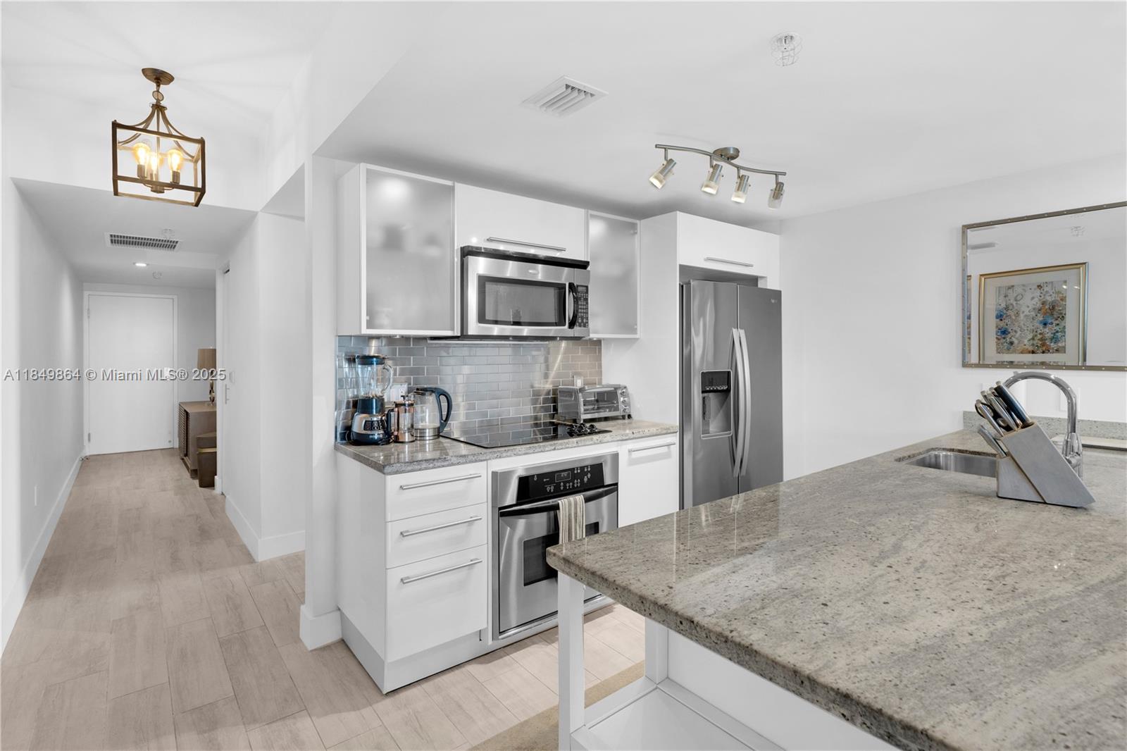 A modern kitchen features white cabinets, stainless steel appliances, and a granite-topped island — 185 SW 7th St # 1901, Miami FL 33130, MIAMI, FL