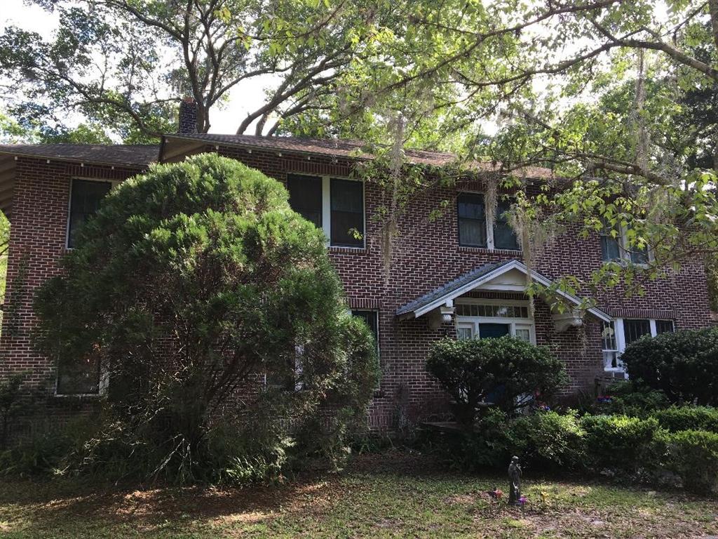 A two-story brick house with a gabled entryway sits behind large trees and shrubs — 635 NE 9TH AVENUE, GAINESVILLE, FL