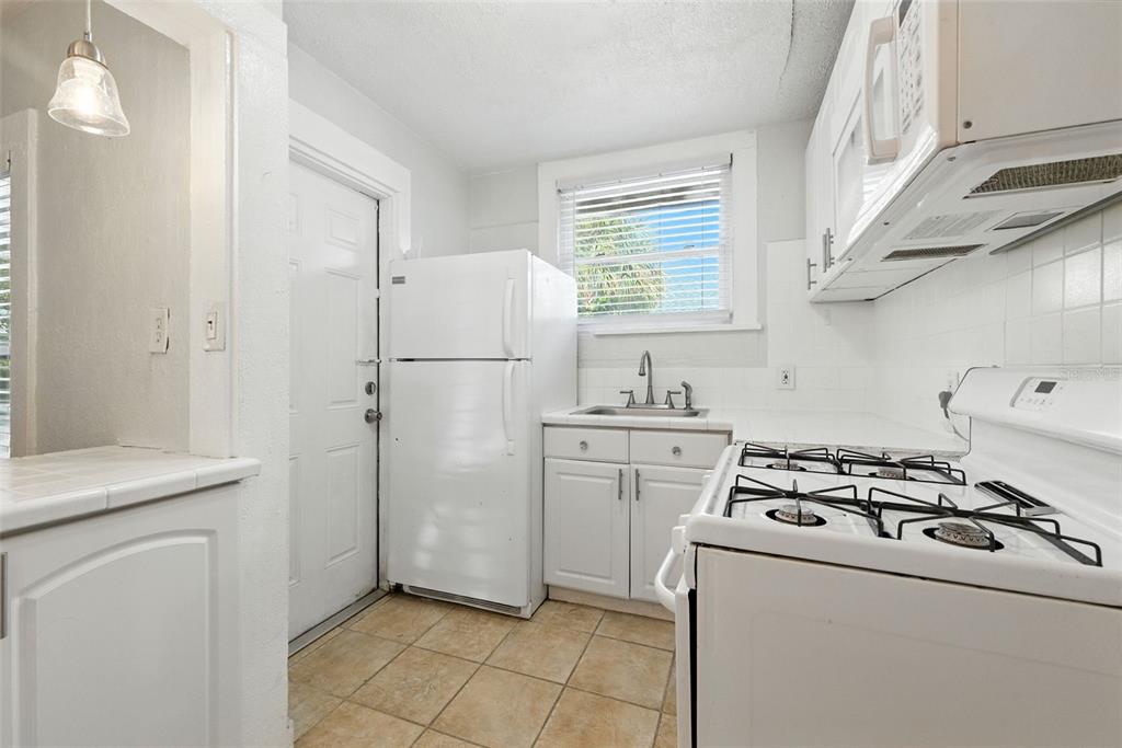 A small kitchen features white cabinets, a gas stove, a refrigerator, and tiled flooring — 1040 19TH AVENUE N, ST PETERSBURG, FL