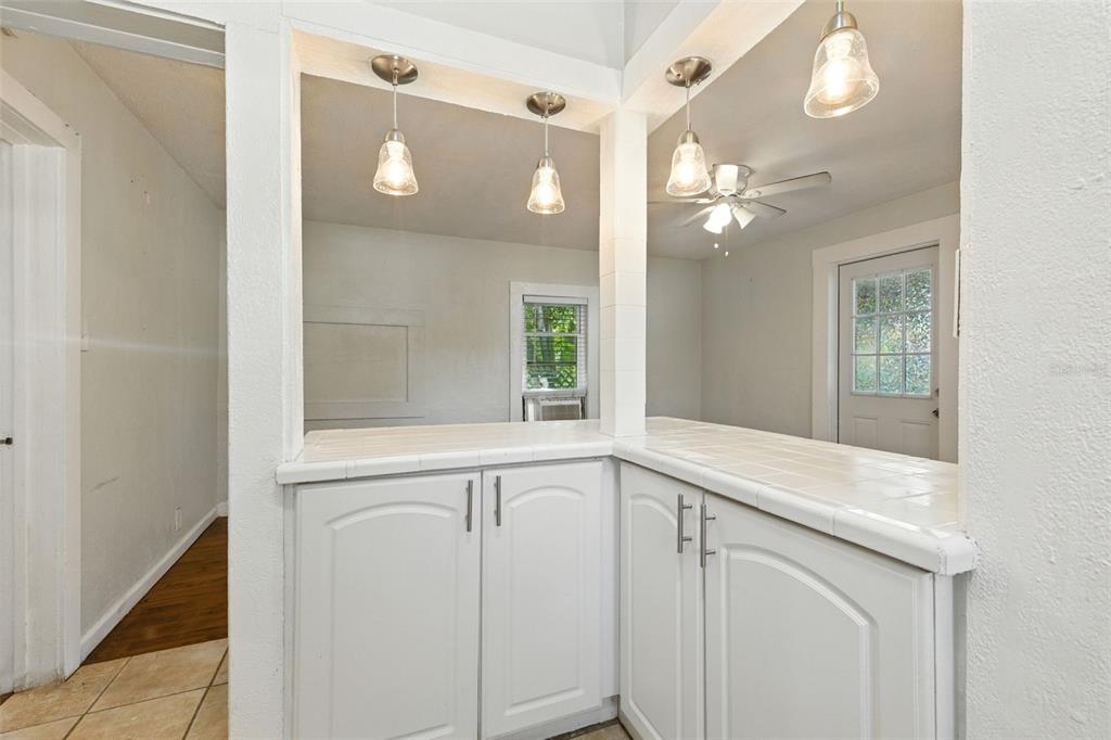 A white kitchen pass-through counter with tiled surfaces, lower cabinets, and hanging pendant lights — 1040 19TH AVENUE N, ST PETERSBURG, FL
