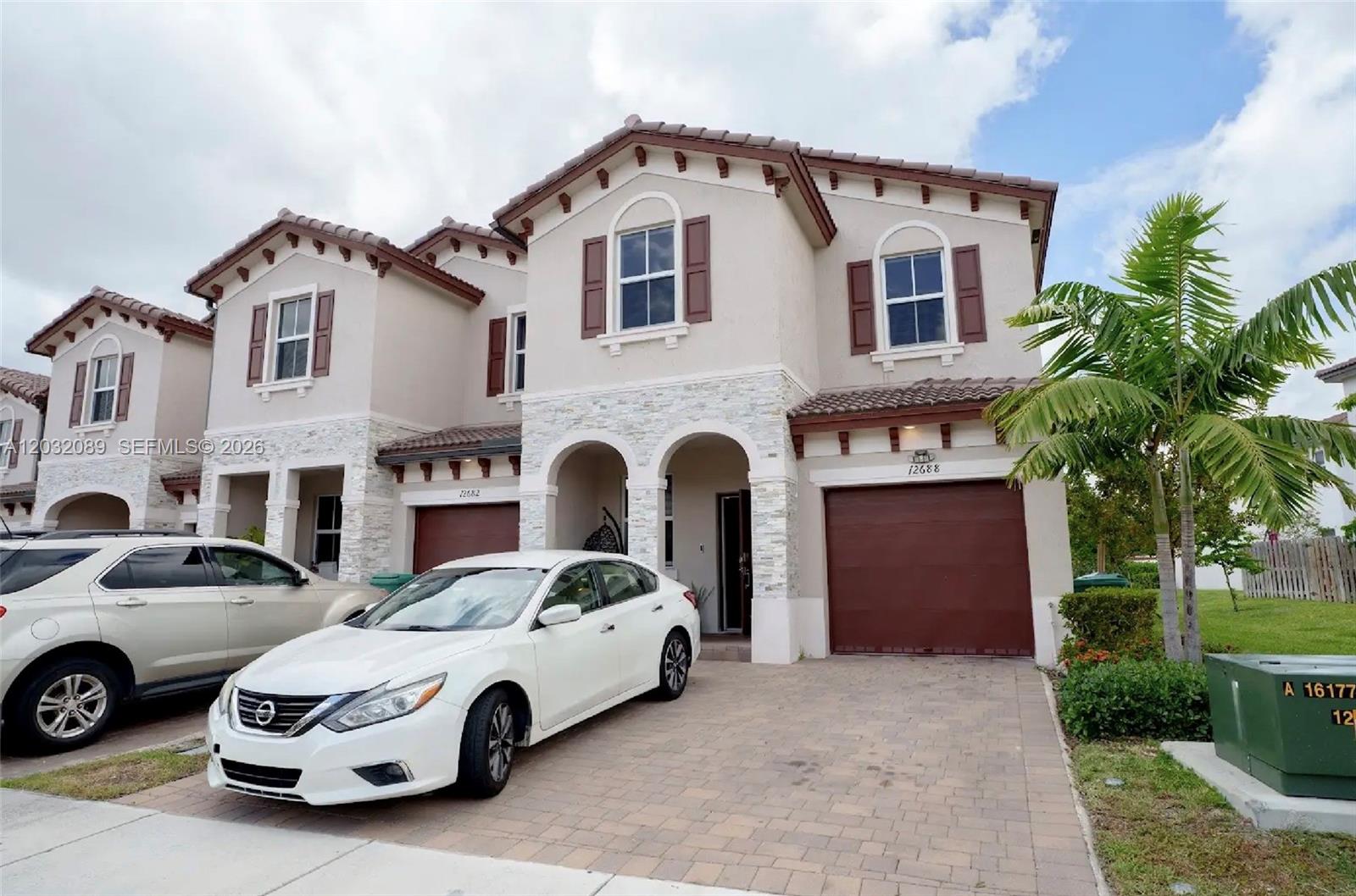 A two-story suburban townhouse with a stone facade, brown shutters, and a paved driveway — 12688 NW 23rd Pl, Miami FL 33167, MIAMI, FL
