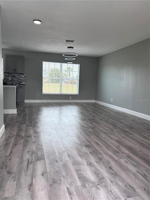An open-concept living area features gray walls, wood-look flooring, and a modern tiered chandelier — 134 PANSY COURT, KISSIMMEE, FL