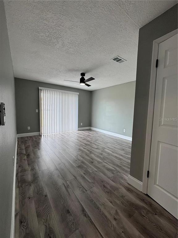 An empty room features gray walls, wood-look flooring, a ceiling fan, and vertical window blinds — 134 PANSY COURT, KISSIMMEE, FL