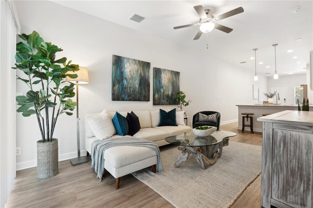 A living room with a sectional sofa, glass coffee table, and open kitchen in background — 7616 WASHINGTON STREET, PORT RICHEY, FL