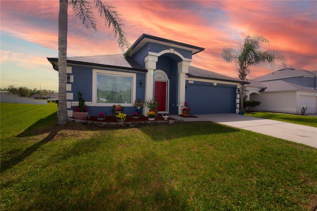 A blue single-story house with a red front door and a two-car garage at sunset — 25500 GEDDY DRIVE, LAND O LAKES, FL