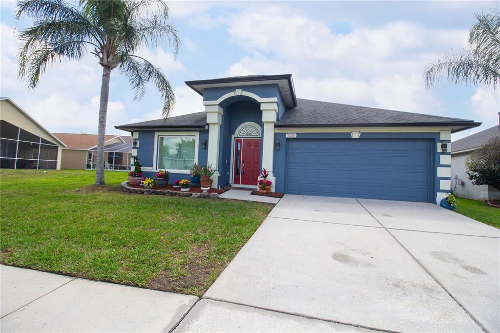 A blue single-story house with a red front door, a two-car garage, and palm trees — 25500 GEDDY DRIVE, LAND O LAKES, FL