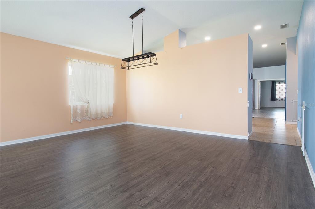A dining room with dark wood-look flooring, peach walls, and a rectangular metal light fixture — 25500 GEDDY DRIVE, LAND O LAKES, FL