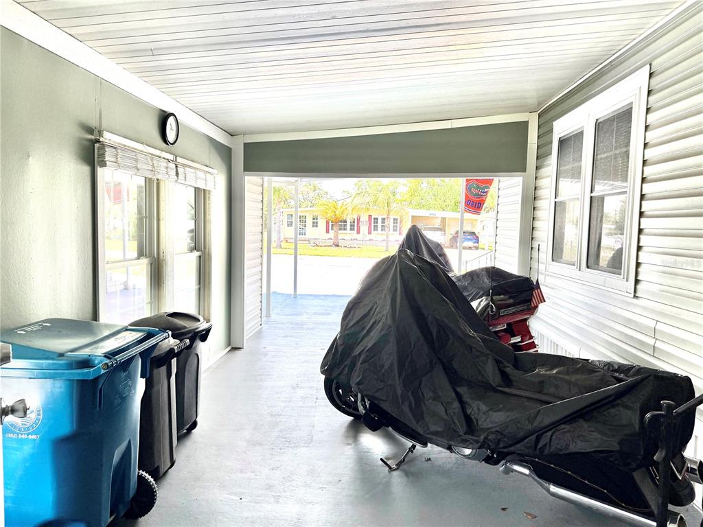 A covered carport features a concrete floor, two trash bins, and a motorcycle under a cover — 12176 EVANTIDE AVENUE, BROOKSVILLE, FL