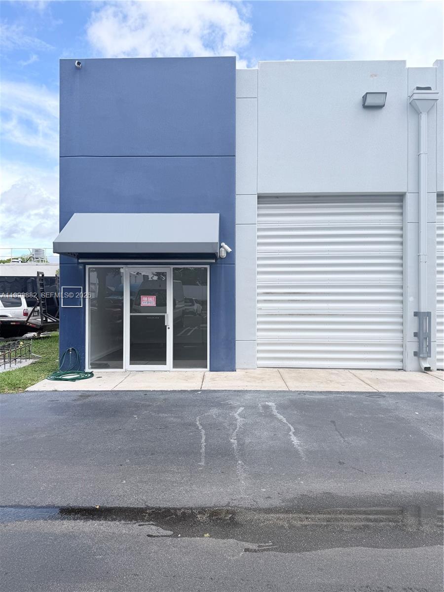 The exterior of a commercial warehouse unit features a blue facade, glass entrance, and roll-up door — 13210 SW 132 Ave Unit 1C, Miami FL 33186, MIAMI, FL