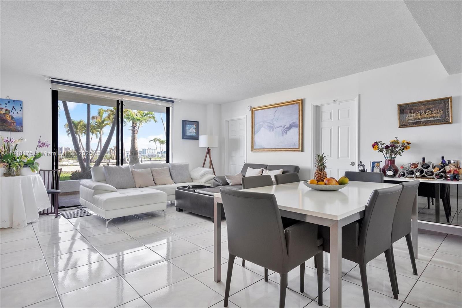 A bright living and dining area features white tile floors, a sectional sofa, and floor-to-ceiling windows — 13499 Biscayne Blvd # 406, North Miami FL 33181, NORTH MIAMI, FL
