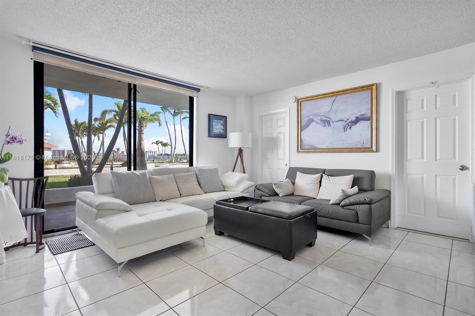 A living room features white tile floors, a white sectional, a gray sofa, and large windows — 13499 Biscayne Blvd # 406, North Miami FL 33181, NORTH MIAMI, FL