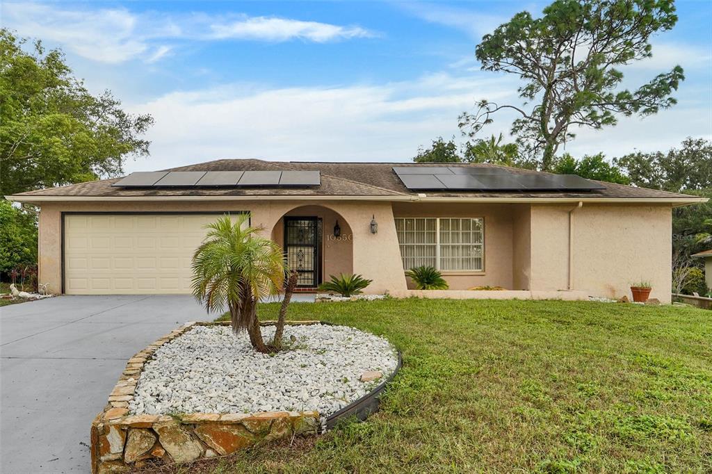 A single-story house with a beige stucco exterior, a two-car garage, and rooftop solar panels — 10550 CALICO LOOP, PORT RICHEY, FL