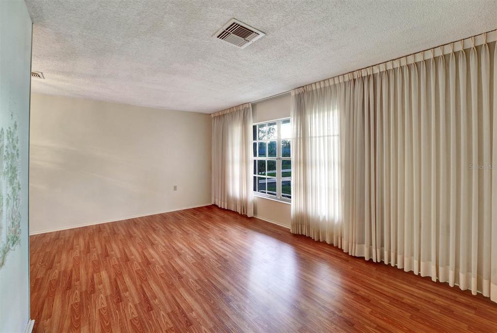 An empty room features wood-look flooring, light-colored walls, and floor-to-ceiling curtains covering a window — 10550 CALICO LOOP, PORT RICHEY, FL