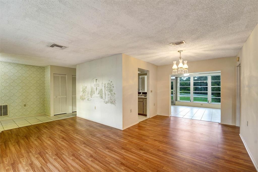 A living room with wood-look flooring, a central wall mural, and a view into a sunroom — 10550 CALICO LOOP, PORT RICHEY, FL