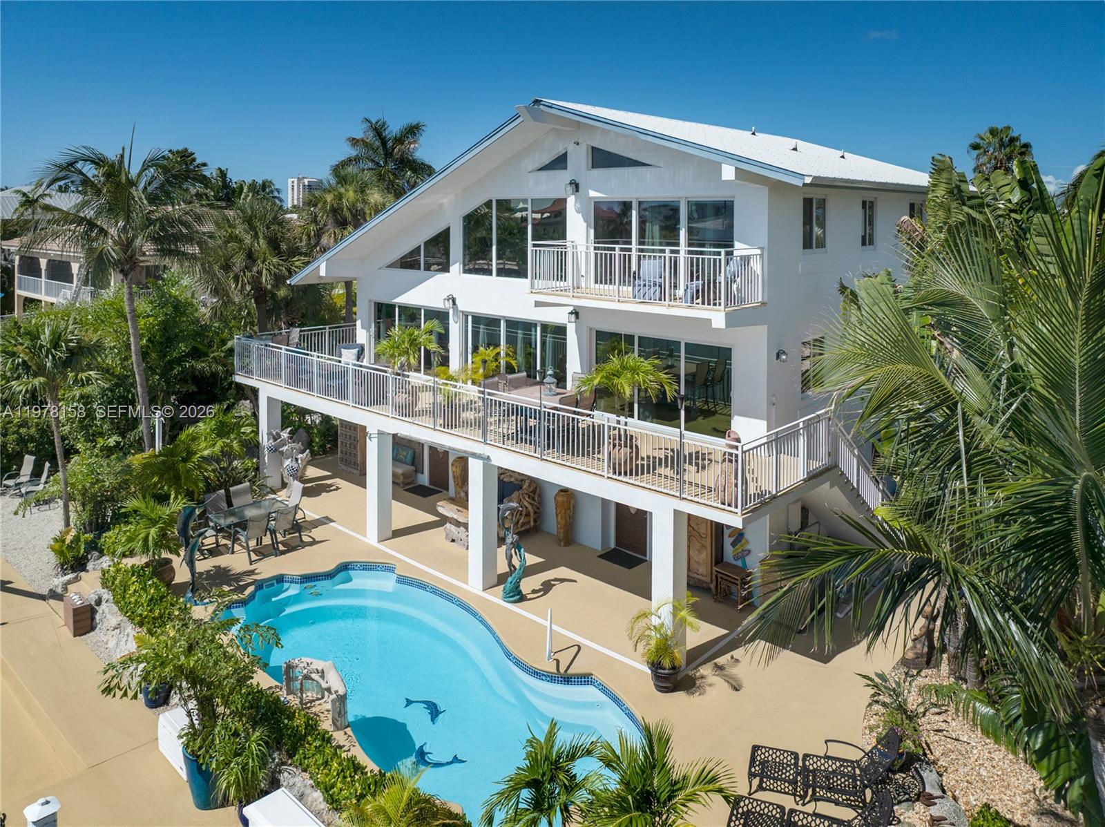 An elevated white house with multiple balconies overlooks a swimming pool in a tropical setting — 14 Avenue F, Marathon FL 33050, MARATHON, FL